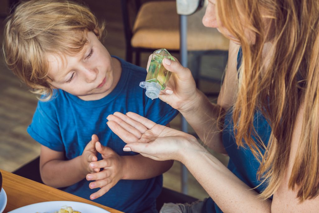 Two children use a green bottle of hand sanitizer. Concept of hand sanitizers being safe for children. 