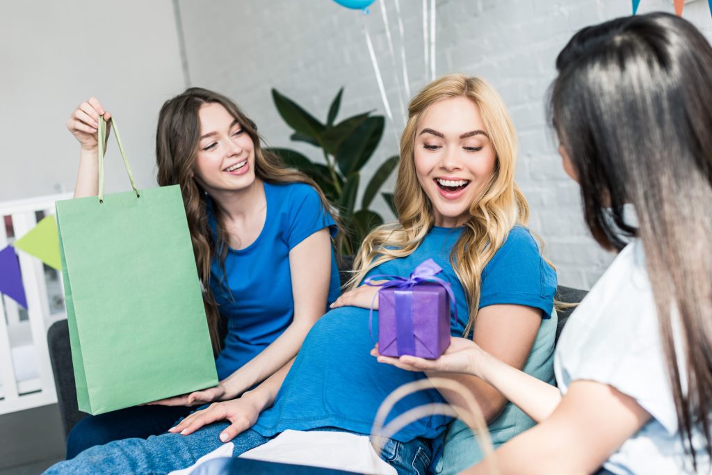 A pregnant woman receiving gifts from her friends during a baby shower.