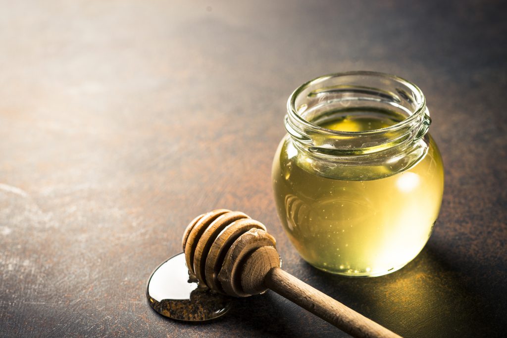 A glass jar full of honey alongside a dipper. Honey is a popular home remedy to get glowing skin. 