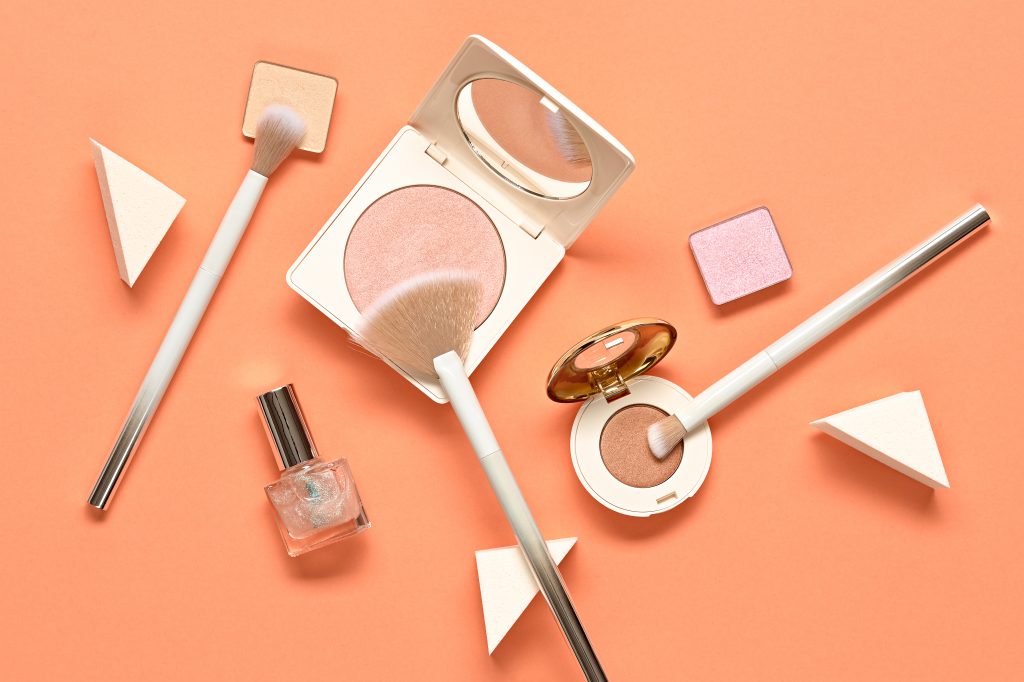 Vegan makeup products scattered against a peach colored background. 