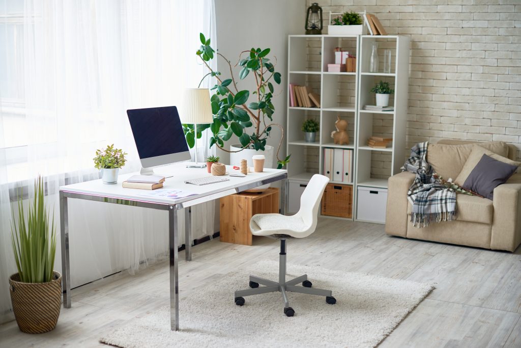 A cozy and comfortable modern home office with a desk, chair, bookshel, sofa chair, and big windows,