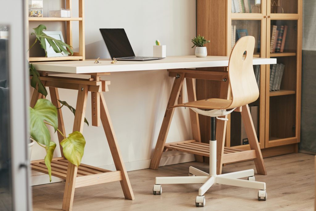 A modern home office with a desk against a wall, a chair, a bookshelf, and a few plants. Plants are great for any office space. 