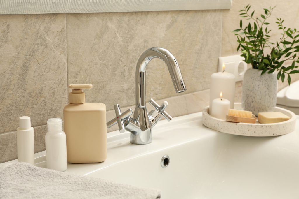 Bathroom accessories near a sink. Soap dispensers, candles, plant in a ceramic vase, soaps, and lotions. 