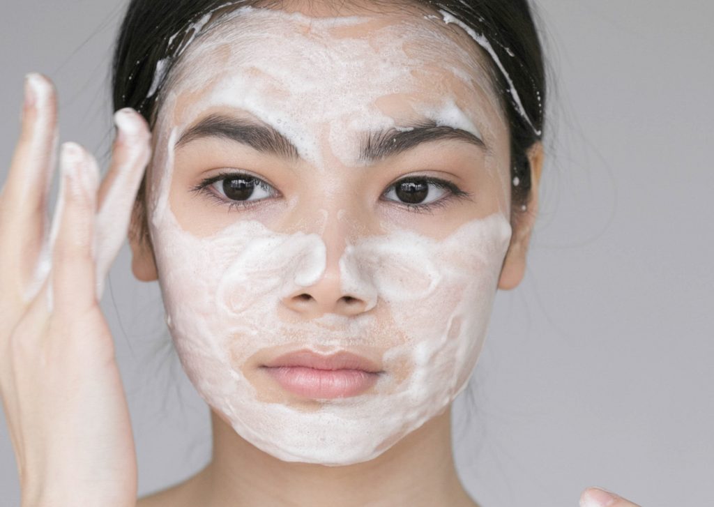 A young woman cleaning her face using face wash, with her entire face covered in lather. It is important to avoid harmful ingredients like alcohol that are commonly found in face washes.