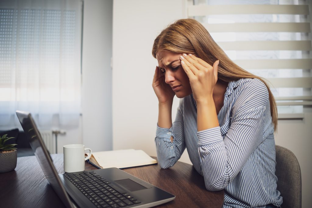 A business woman at her desk pressing her forehead and frowning, demonstrating stress. A lot of stress can lead to acne and other skin issues. 