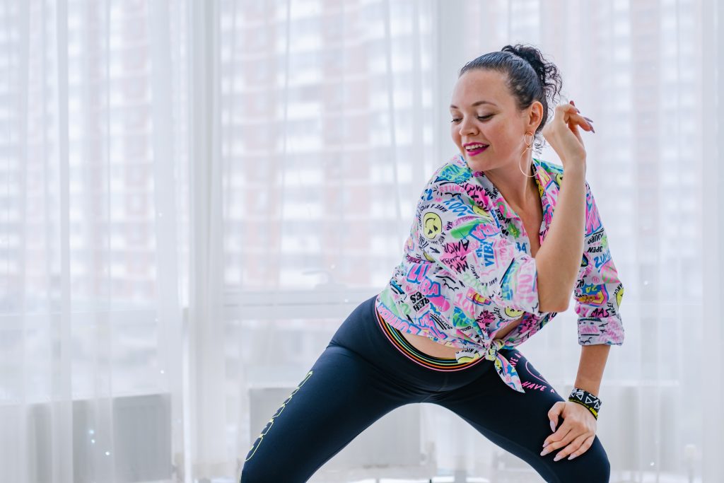 A happy woman does zumba at home to stay active. White curtains in the background.