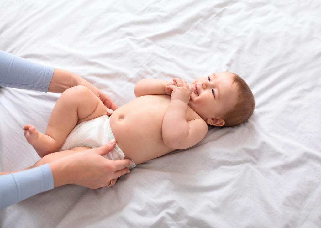 A mother changing her baby's diaper. Baby lying on a white bedcover. 