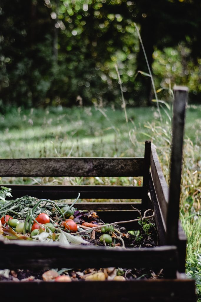 A wooden compost pit in the garden with kitchen waste in it. Concept of composting, vegetable waste, sustainable living, and natural fertilizers.